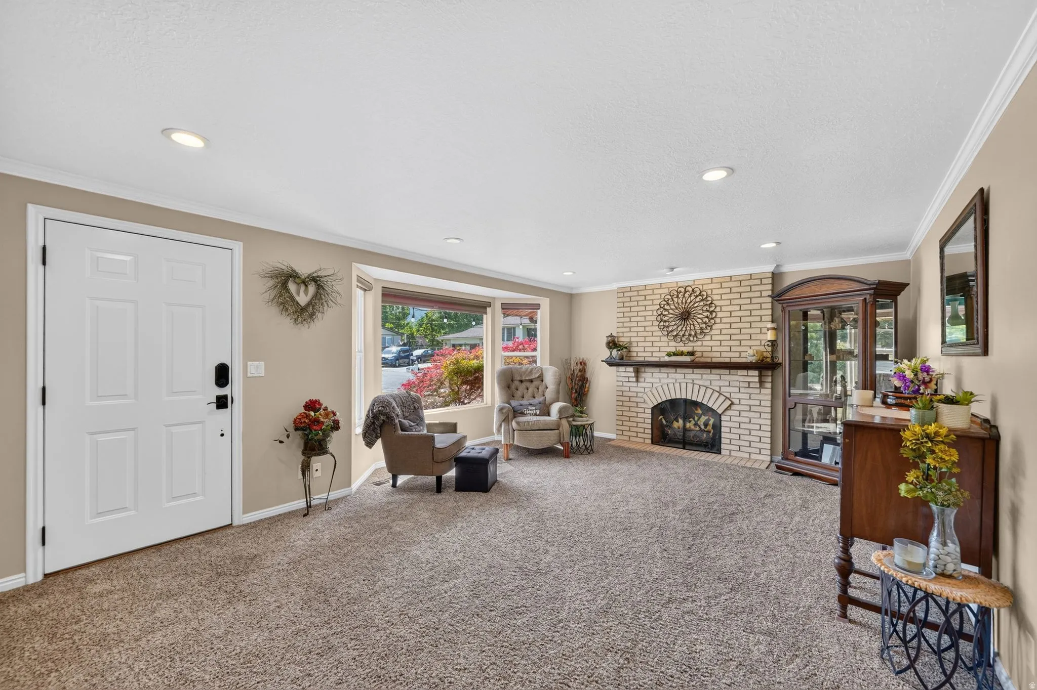 Spacious living area featuring a brick fireplace with a wood mantle, a large bay window, recessed lighting, and crown molding