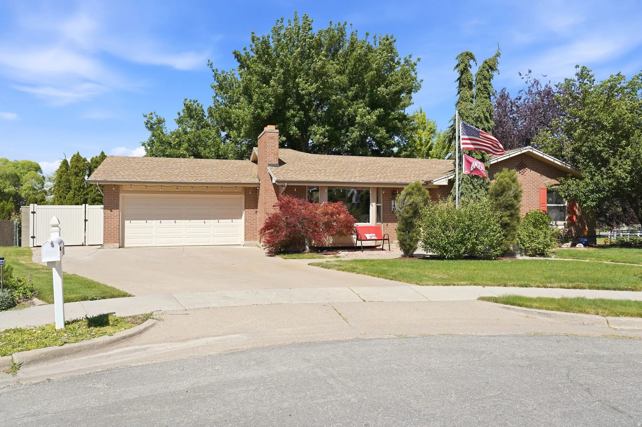 Brick-front residence featuring a two-car garage, mature landscaping, a concrete driveway, and a front porch area with a bay window