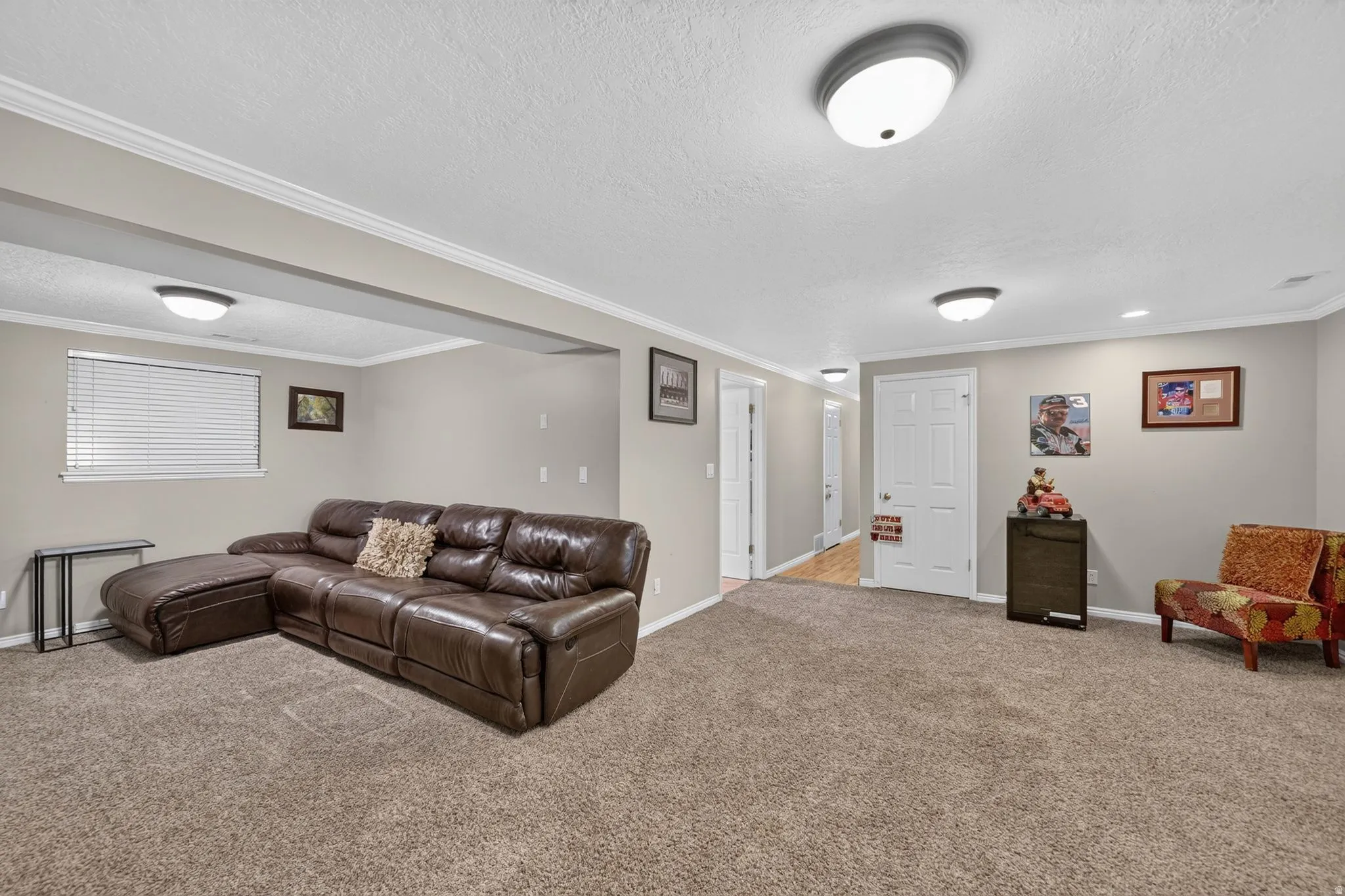 Spacious living area featuring neutral-toned walls, crown molding, and plush carpet flooring
