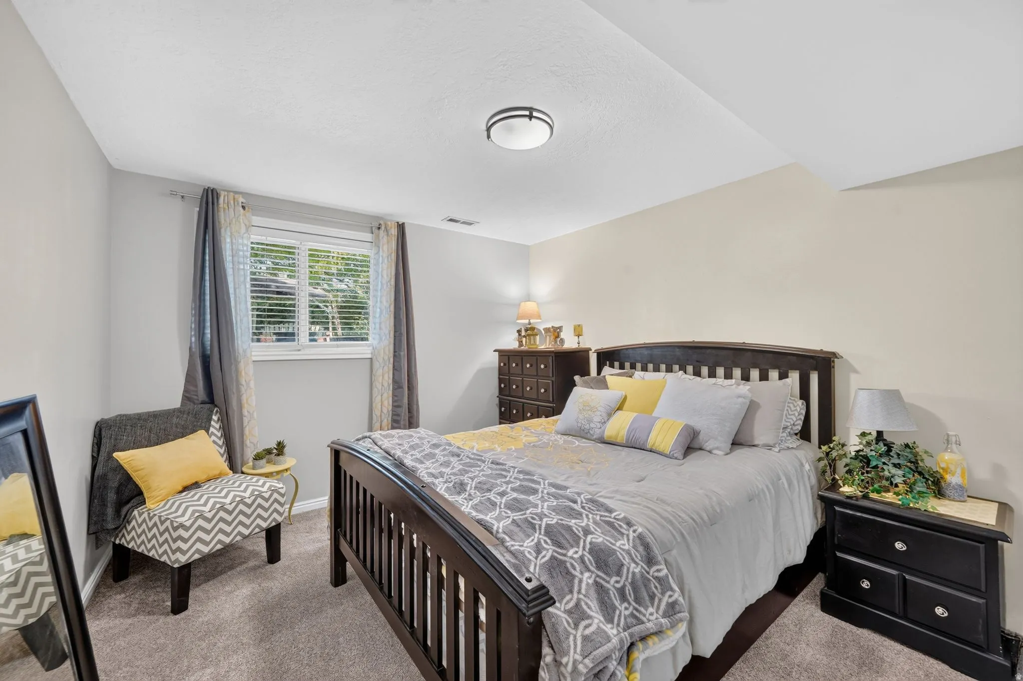 Carpeted room featuring a window with blinds, a dark wood-finish bed frame, and a flush-mount ceiling light