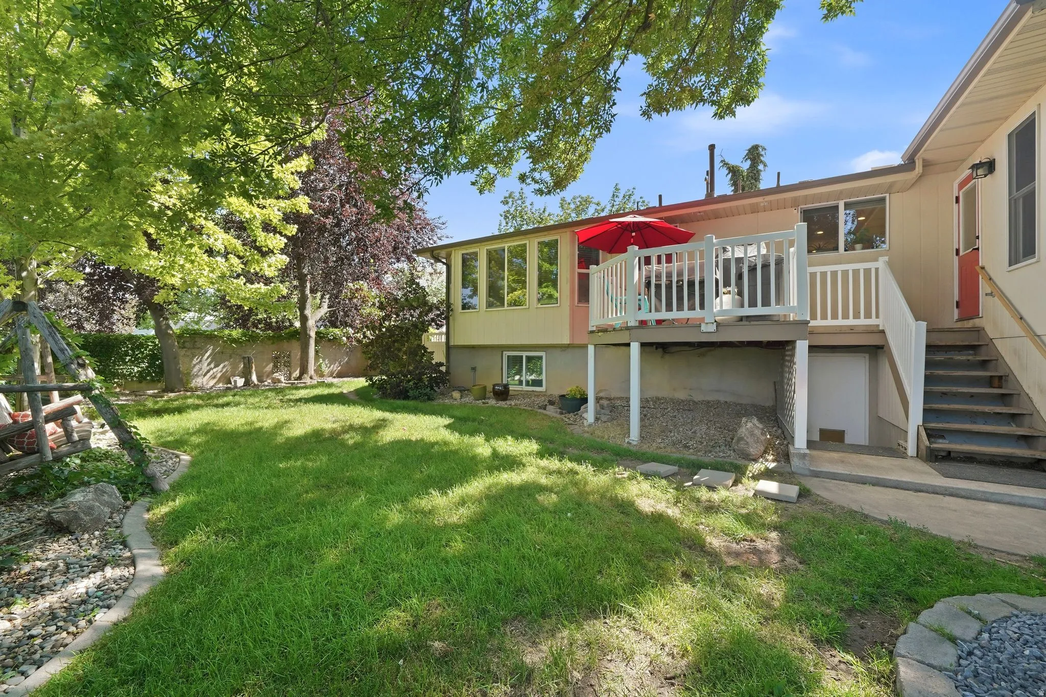 Expansive backyard featuring a manicured lawn, mature trees, and a wooden deck with white railings