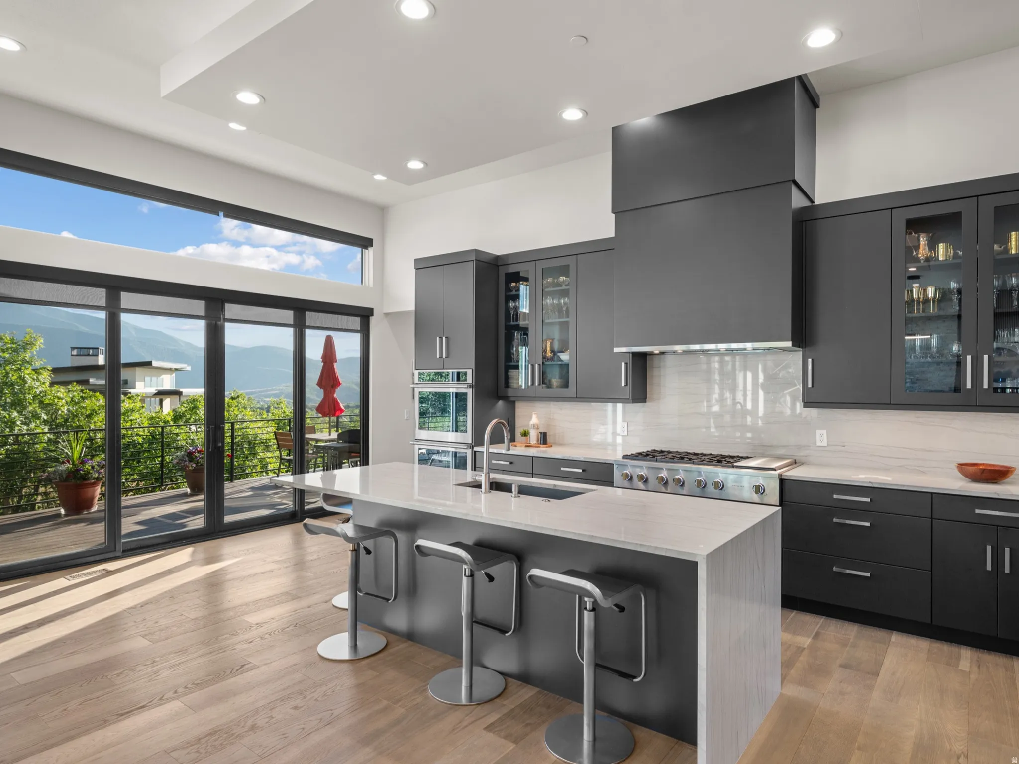 Modern kitchen featuring dark cabinetry, stainless steel appliances, and quartz waterfall countertops