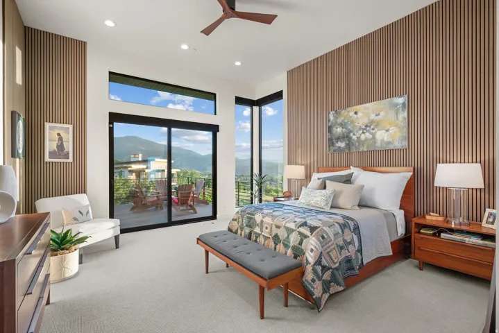 Primary bedroom featuring a slatted wood  accent walls, ceiling fan, recessed lighting, and a large sliding glass door with transom window above