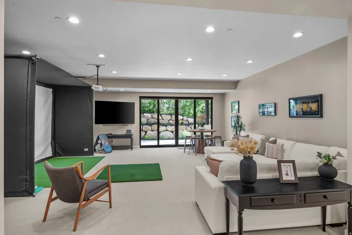 Spacious lower-level entertainment area featuring recessed lighting, a golf simulator with projector, and expansive glass sliding doors leading to the back patio