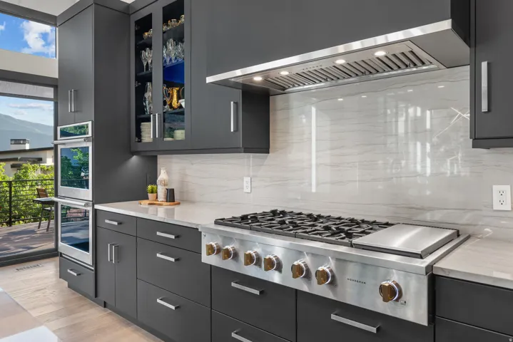 Sleek kitchen featuring dark cabinetry, stainless steel double ovens, a professional-grade gas range, and quartz countertops and matching backsplash