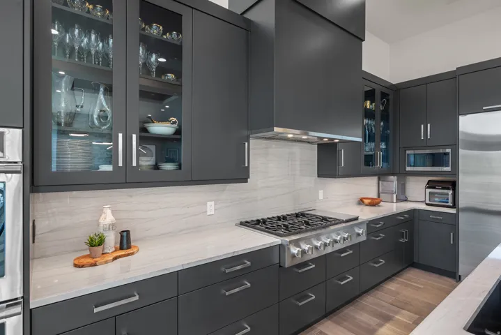 Contemporary kitchen featuring dark cabinetry with glass, stainless steel appliances, quartz countertops and backsplash.