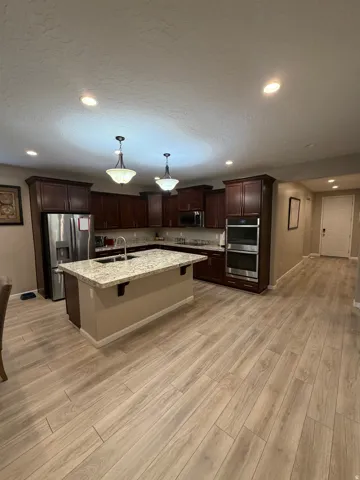 Kitchen featuring dark wood cabinetry, a central island with a light-toned countertop, stainless steel appliances, and wood-finish flooring