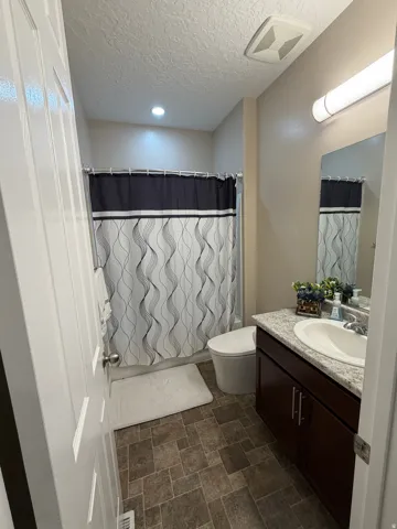Bathroom featuring an integrated bathtub and shower with a tile surround, a dark wood-finish vanity with a light speckled countertop, an undermount sink, and durable tile flooring