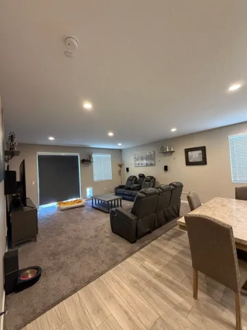 Spacious living area featuring recessed lighting, a large sliding glass door, and multiple windows with blinds