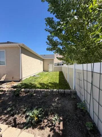Expansive backyard space featuring a manicured lawn, established garden bed with concrete block edging, and a vinyl privacy fence