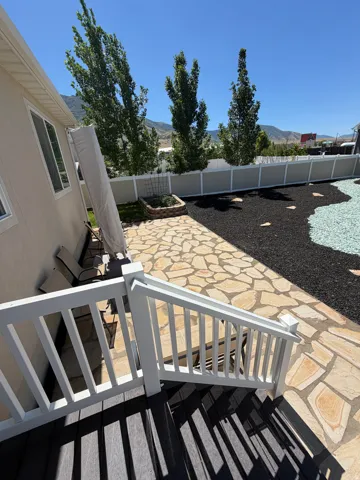 Paver patio area featuring a stone planter, decorative landscaping, and a white fence