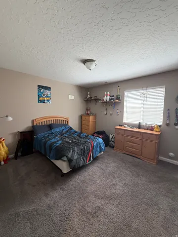 Carpeted room with a textured ceiling and a window featuring horizontal blinds