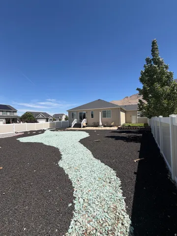 Landscaped backyard featuring black lava rock and a winding light green decorative rock pathway