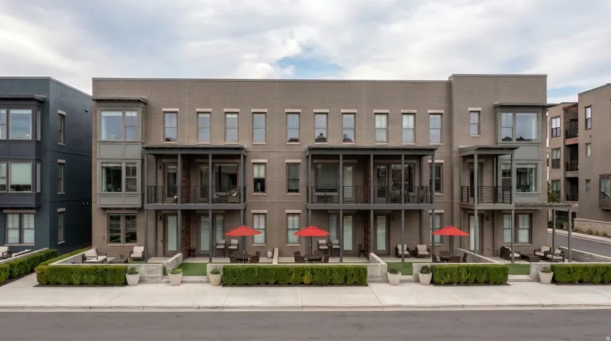 Modern multi-story brick facade featuring private ground-level patios with green space, second-story balconies, and large windows