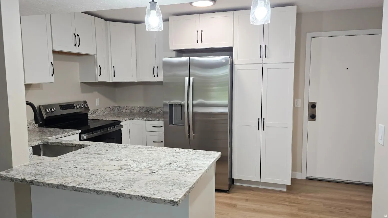 Updated kitchen featuring white shaker cabinetry, stainless steel appliances, speckled countertops, a double basin sink, and wood-finish flooring