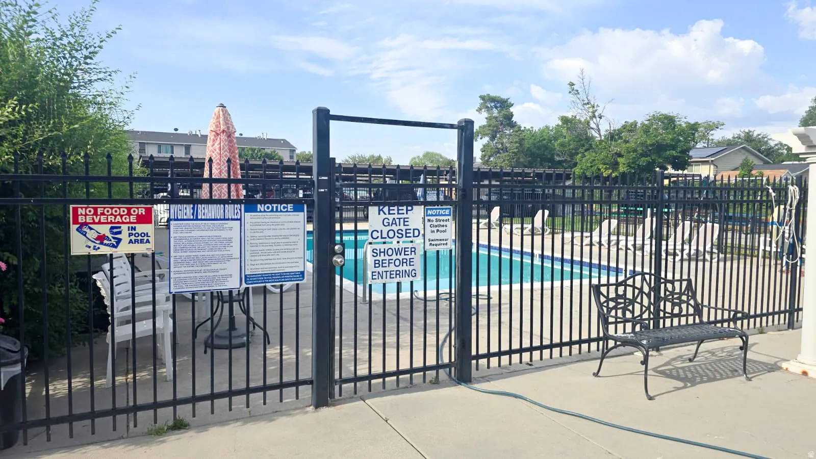 Secured outdoor swimming pool area featuring a perimeter fence, concrete decking, and sun loungers