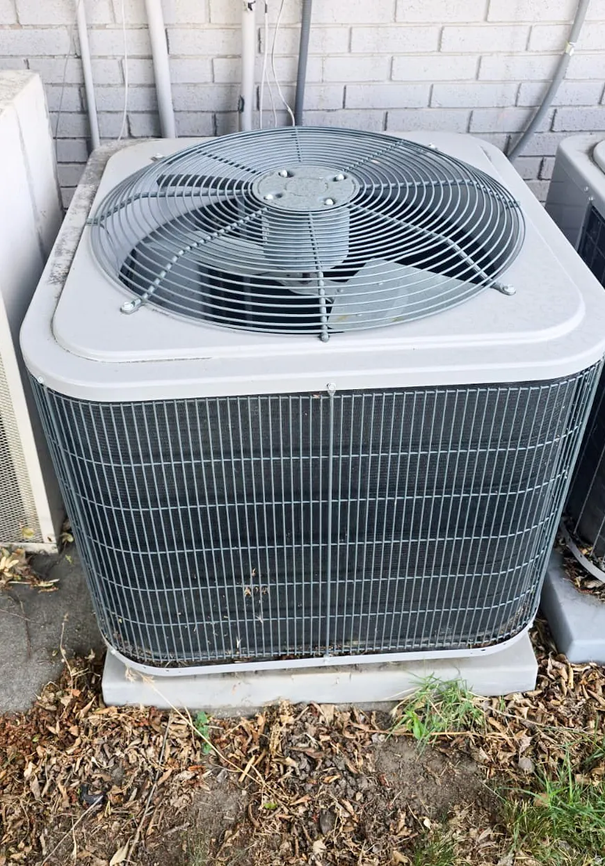 Outdoor HVAC unit featuring a top-mounted fan, protective grille, and a concrete pad foundation