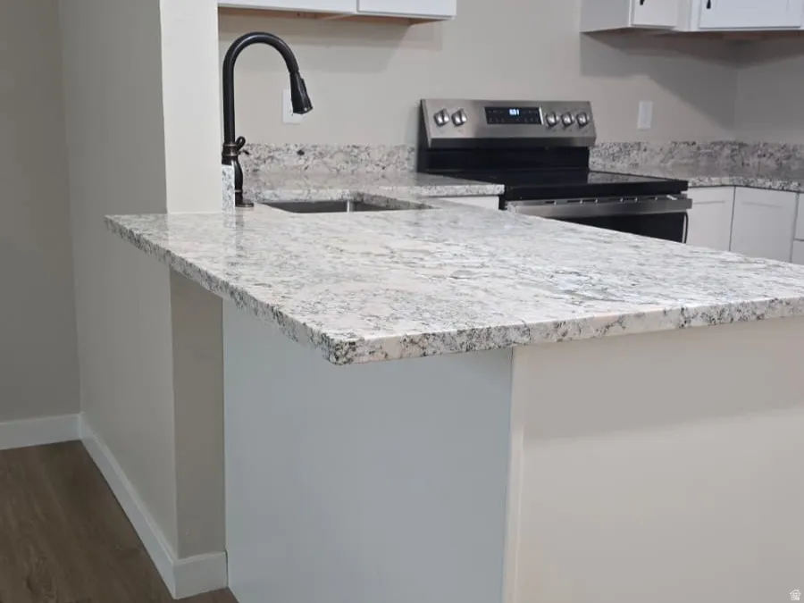 Kitchen island with light-toned granite countertop, featuring a black gooseneck faucet and undermount sink