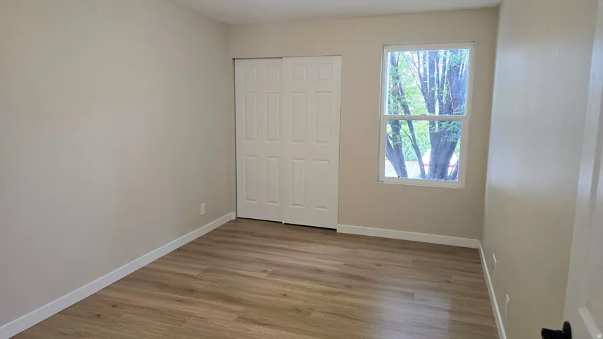 Neutral-toned interior room featuring wood-finish flooring, a double-paned window, and a closet with bifold doors