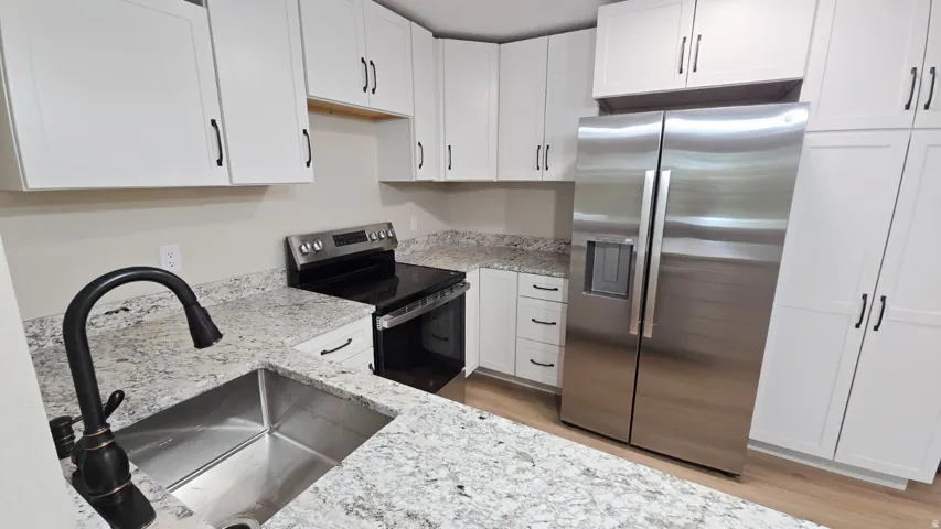 Kitchen featuring extensive white cabinetry, speckled stone countertops, a stainless steel sink with a dark bronze faucet, a stainless steel range, and a stainless steel side-by-side refrigerator