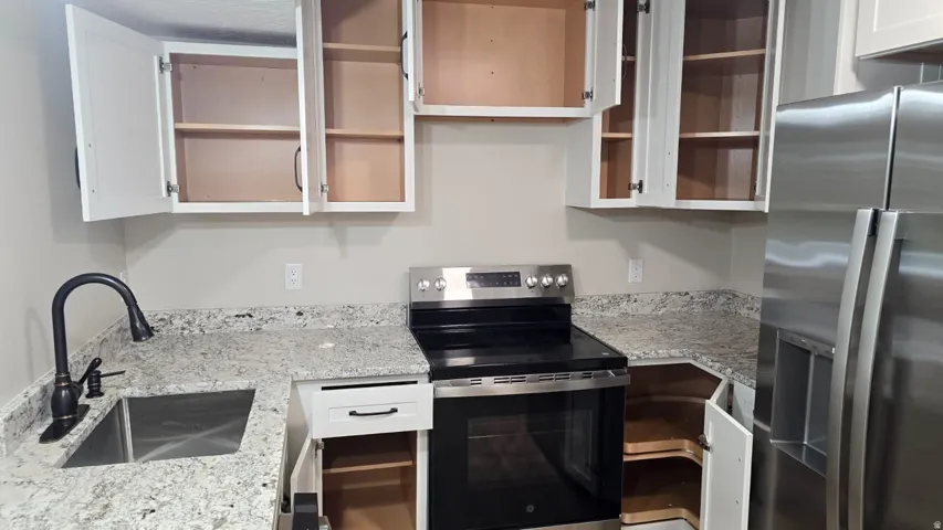 Kitchen featuring white cabinetry, light-toned countertops, a stainless steel sink with a matte black faucet, and stainless steel appliances