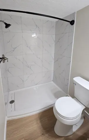 White tile shower surround with grey veining, brushed nickel shower fixtures, and a curved black shower rod