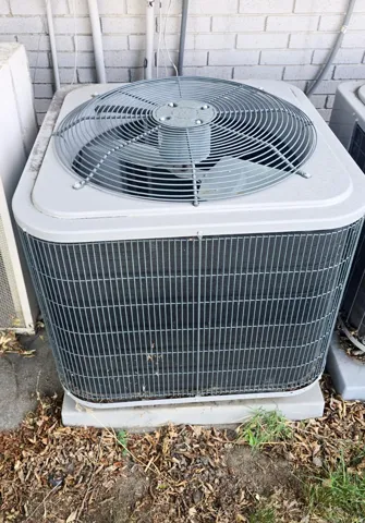 Outdoor HVAC unit featuring a top-mounted fan, protective grille, and a concrete pad foundation