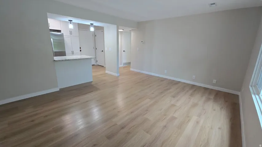 Spacious open-concept living area featuring wood-finish flooring, neutral wall tones, and white baseboards