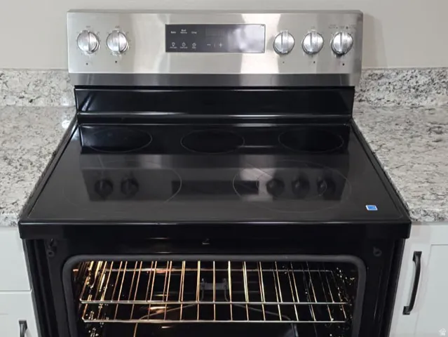 Stainless steel electric range with a black glass cooktop and an integrated lower storage drawer