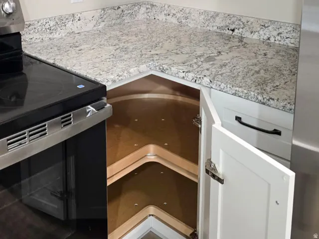 Kitchen corner featuring white shaker-style cabinetry with matte black hardware, light-toned granite countertops, and built-in corner shelving