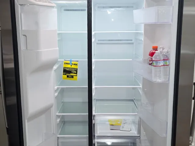 Stainless steel side-by-side refrigerator featuring interior lighting, multiple adjustable glass shelves, clear door bins, and bottom crisper drawers