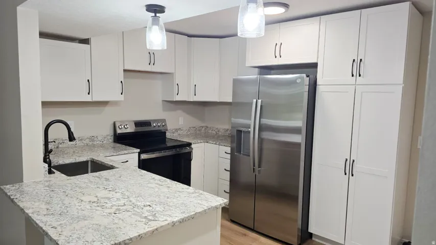 Modern kitchen featuring white shaker cabinetry, stainless steel appliances, speckled countertops, and wood-finish flooring