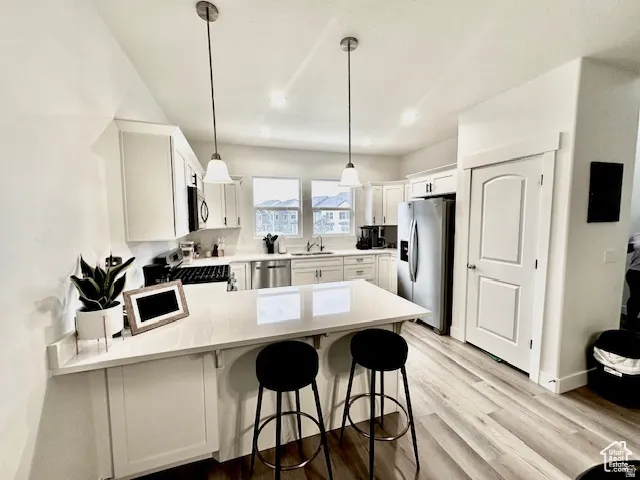 Modern kitchen featuring white shaker cabinetry, stainless steel appliances, light-toned wood-finish flooring, a kitchen island with seating, and pendant lighting