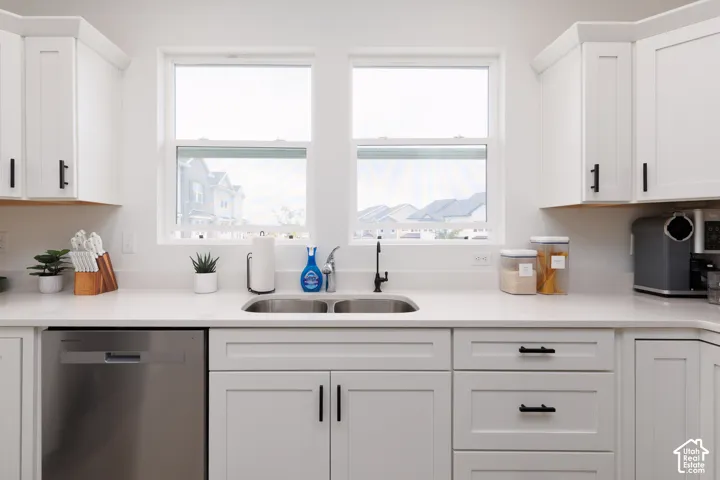 White shaker cabinetry featuring matte black hardware, dual windows, stainless steel undermount sink, a matte black faucet, and light-toned countertops