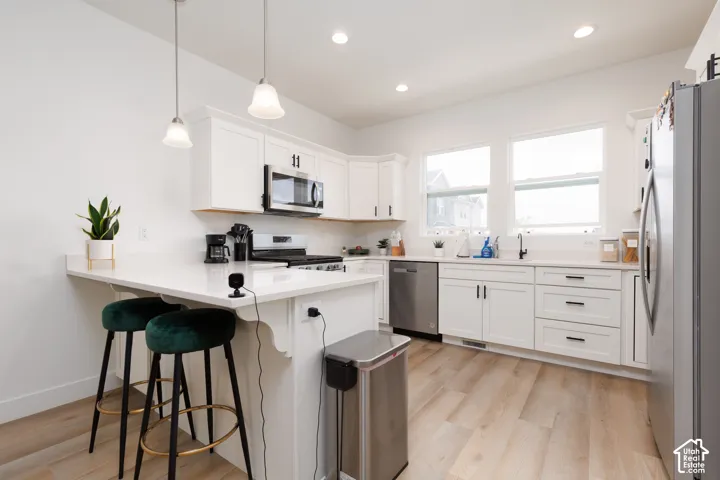 Modern kitchen featuring white cabinetry with dark hardware, a peninsula with pendant lighting, stainless steel appliances, light-toned wood-finish flooring, and recessed ceiling lights