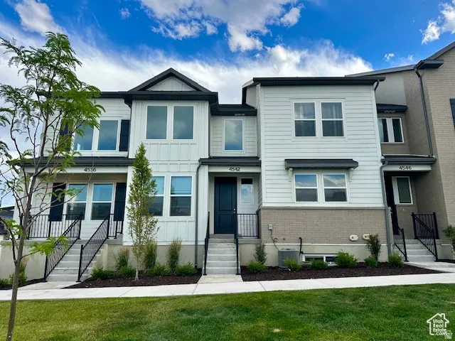 Modern townhome exterior featuring white siding, black trim, and a grey brick foundation