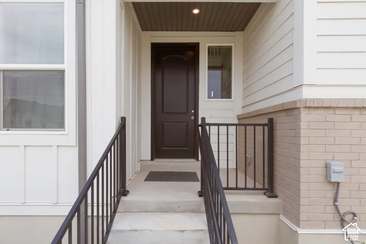 Entryway featuring a dark wood-paneled door, concrete steps, black metal railings, and a side light window