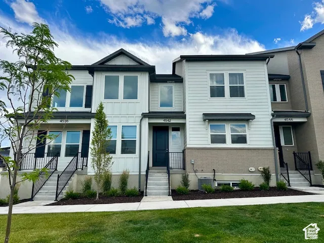 Modern townhome exterior featuring white siding, black trim, and a grey brick foundation