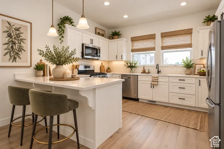 White cabinetry with black hardware, stainless steel appliances, wood-finish flooring, white countertops, and recessed lighting
