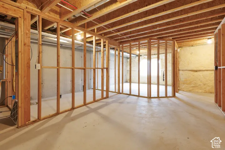 Unfinished basement featuring exposed wood framing, concrete flooring, concrete block walls, and visible ceiling joists