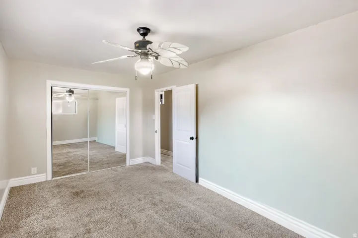 Carpeted room featuring a ceiling fan with light fixture, mirrored closet doors, and a white paneled door
