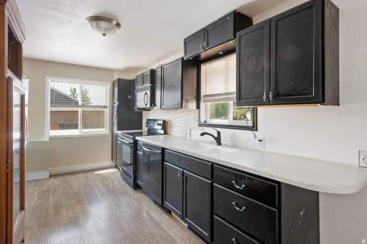 Kitchen featuring black cabinetry, white countertops, stainless steel appliances, and wood-finish flooring