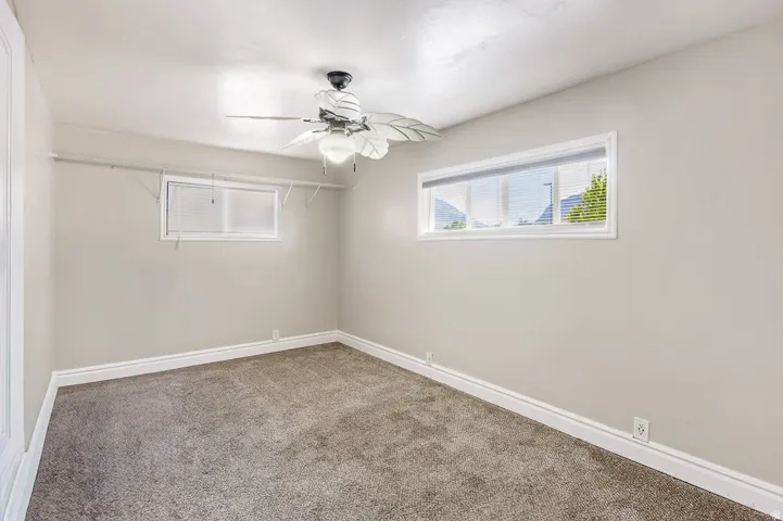 Carpeted interior space featuring light-toned walls, white trim, and a ceiling fan with light fixture
