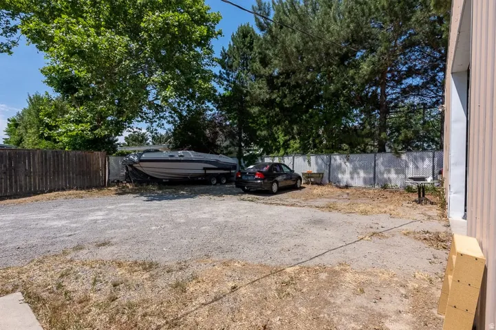 Gravel parking area featuring a privacy fence, mature trees, and ample space for multiple vehicles