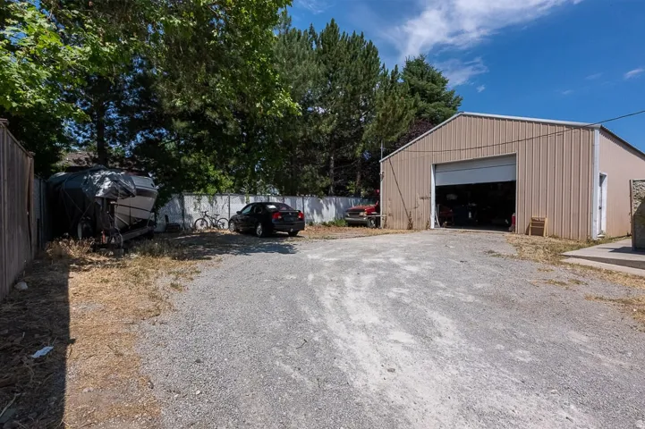 Expansive gravel parking area with a metal industrial-style building featuring a large overhead door