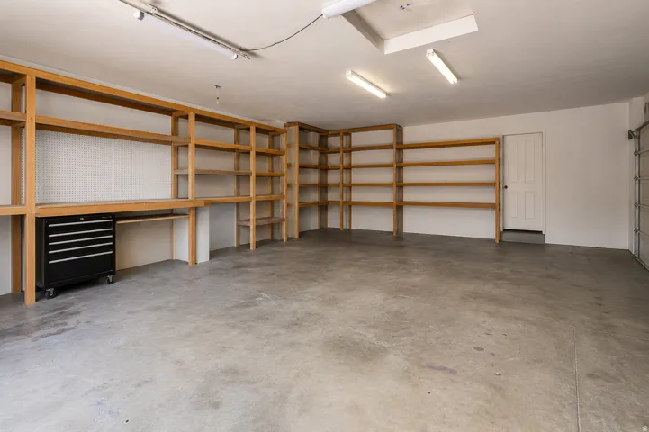 Spacious garage featuring a concrete floor, built-in wooden shelving, pegboard workstation, and a paneled interior door