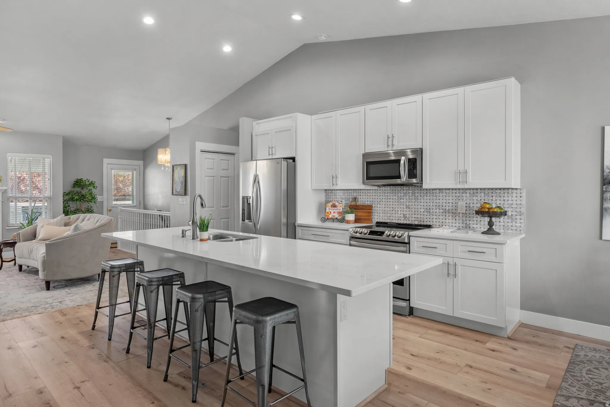 Kitchen featuring a white island with an undermount sink, quartz countertops, stainless steel appliances, and a mosaic tile backsplash