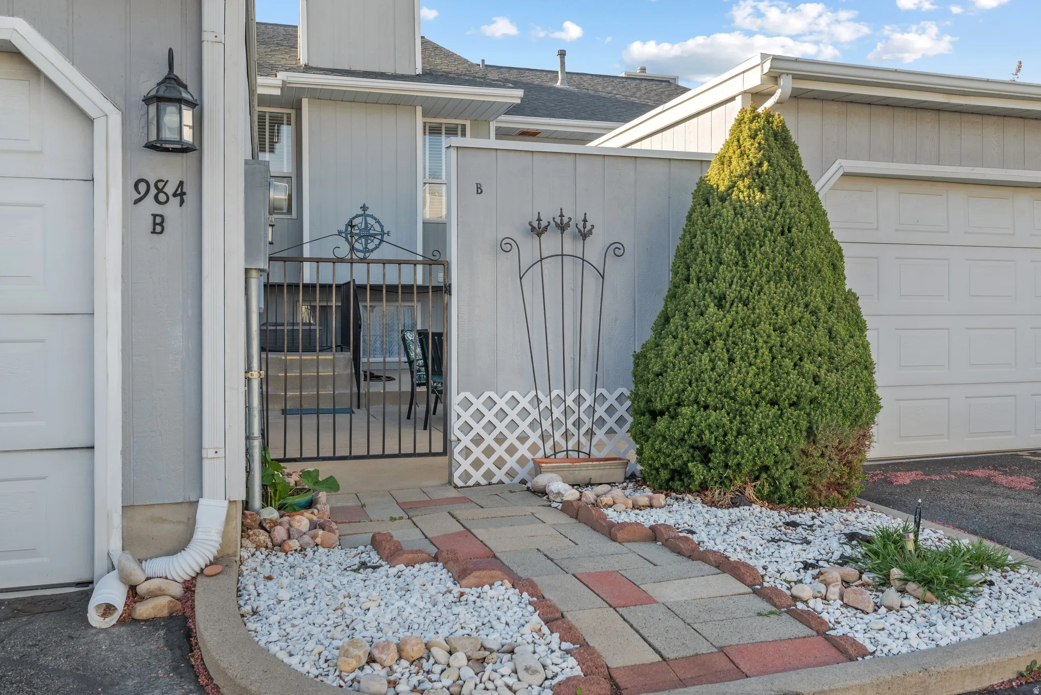 Block paver walkway with a decorative rock border leading to a wrought iron gate and the private patio