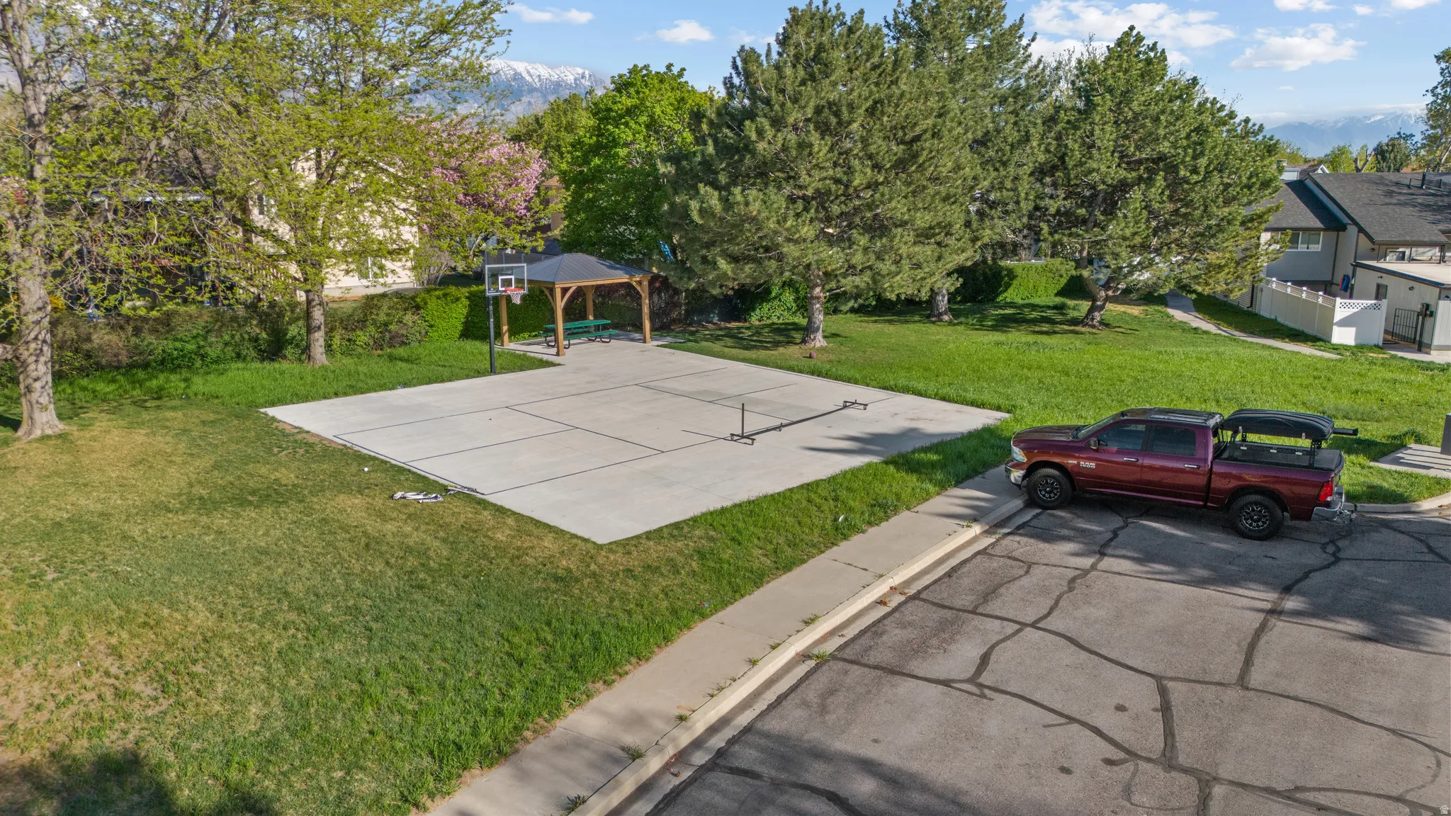 Outdoor recreation area featuring a concrete sports court, a basketball hoop, and a wooden gazebo