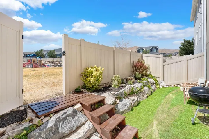 Fenced backyard featuring a manicured lawn, a rock garden with planted shrubs, and a wooden gate providing direct access to an open field